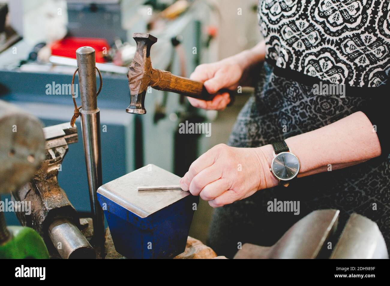 Section médiane de la femme âgée martelant sur le métal pour faire des bijoux en atelier Banque D'Images