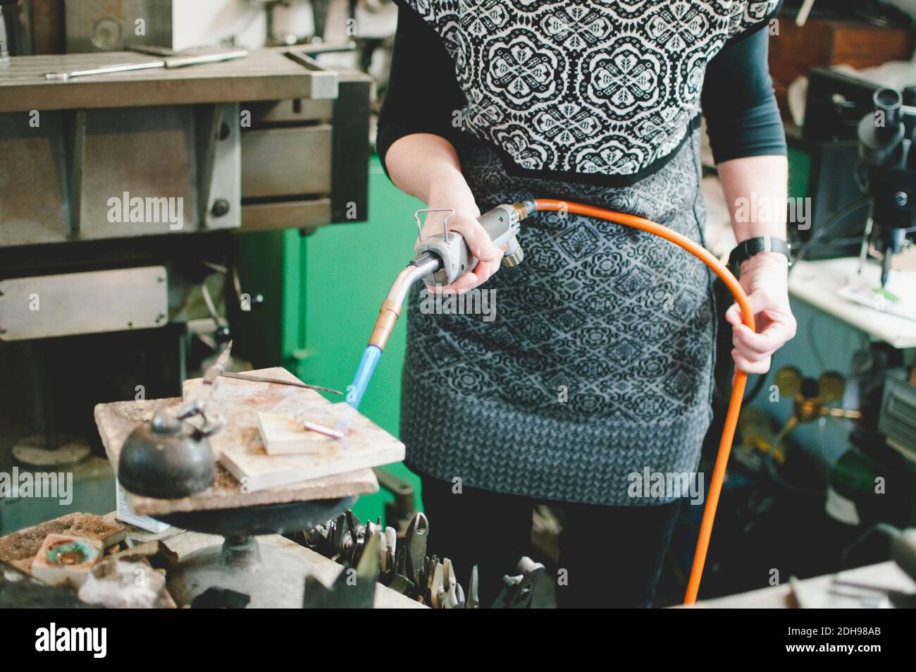 Section médiane d'une femme âgée utilisant un chalumeau pour le travail des métaux dans les bijoux atelier Banque D'Images