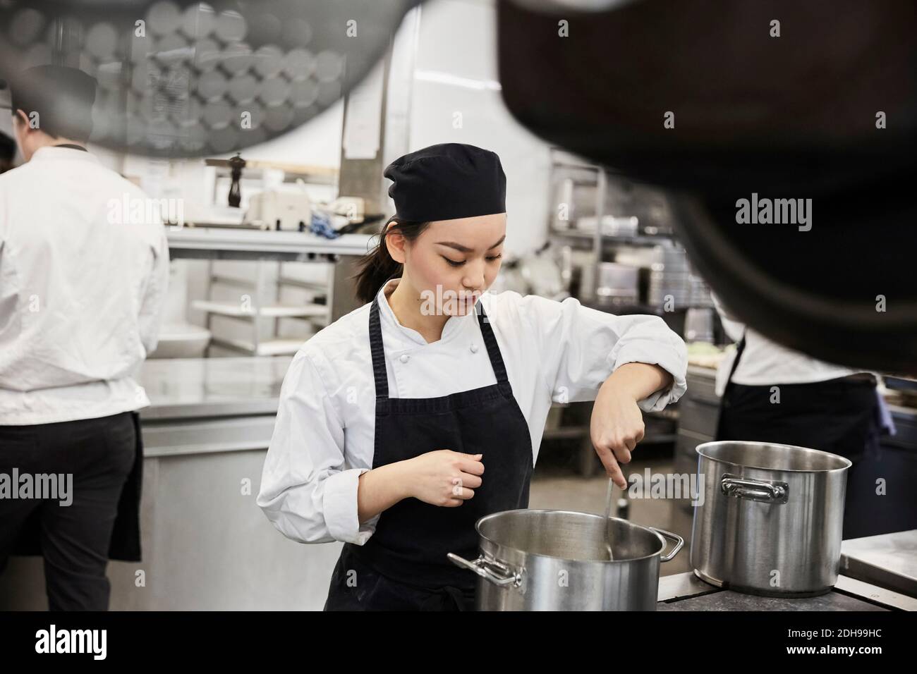 Jeune femme chef remuant la nourriture dans une casserole à la publicité cuisine Banque D'Images