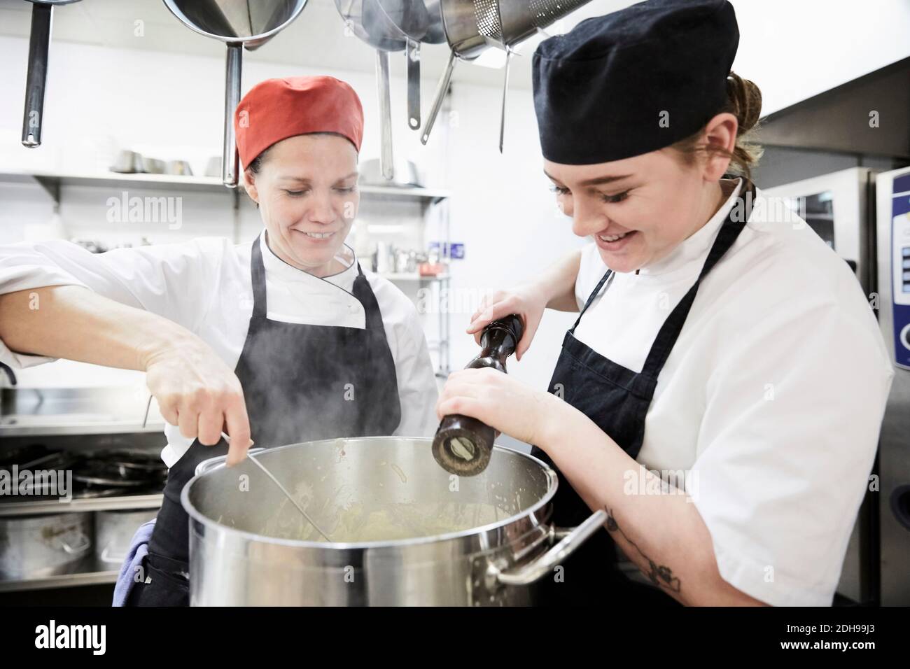 Professeur avec une étudiante de sexe féminin ajoutant du poivre dans une casserole à cuisine commerciale Banque D'Images