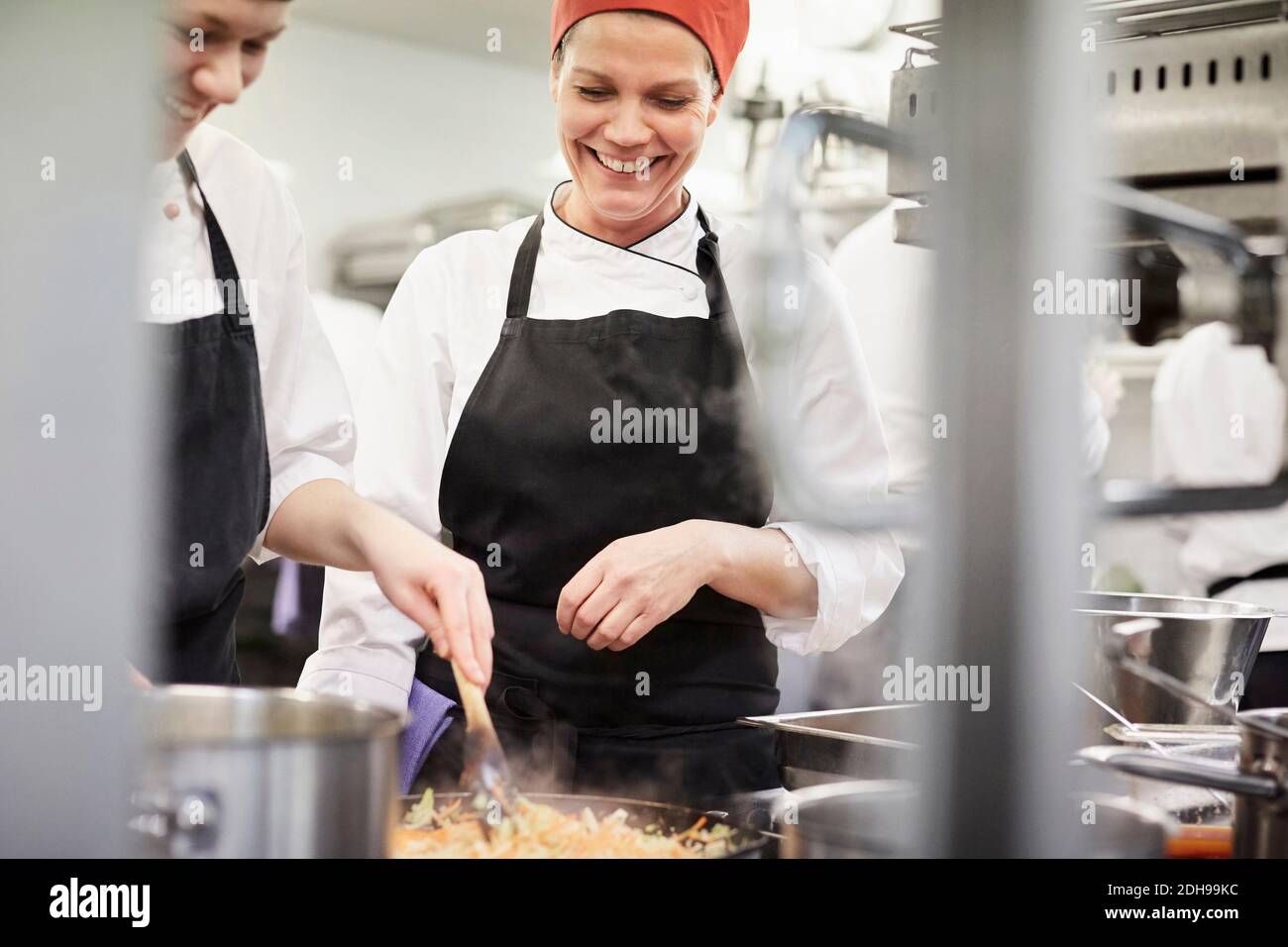 Professeur regardant la femme chef étudiant cuisiner la nourriture dans la cuisine à restaurant Banque D'Images