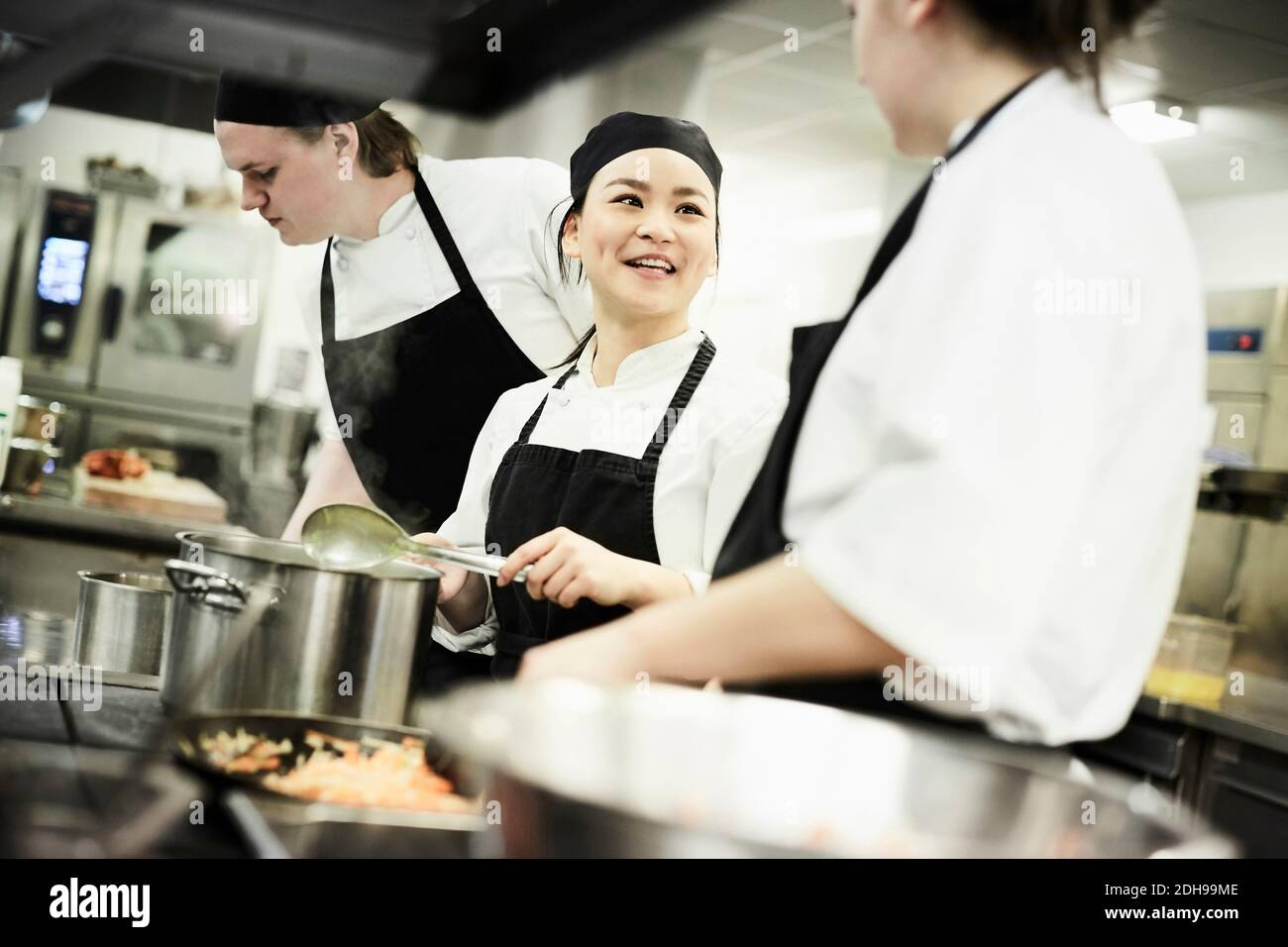 Chef cuisinier féminin cuisant des aliments tout en parlant avec un  collègue dans le commerce cuisine Photo Stock - Alamy