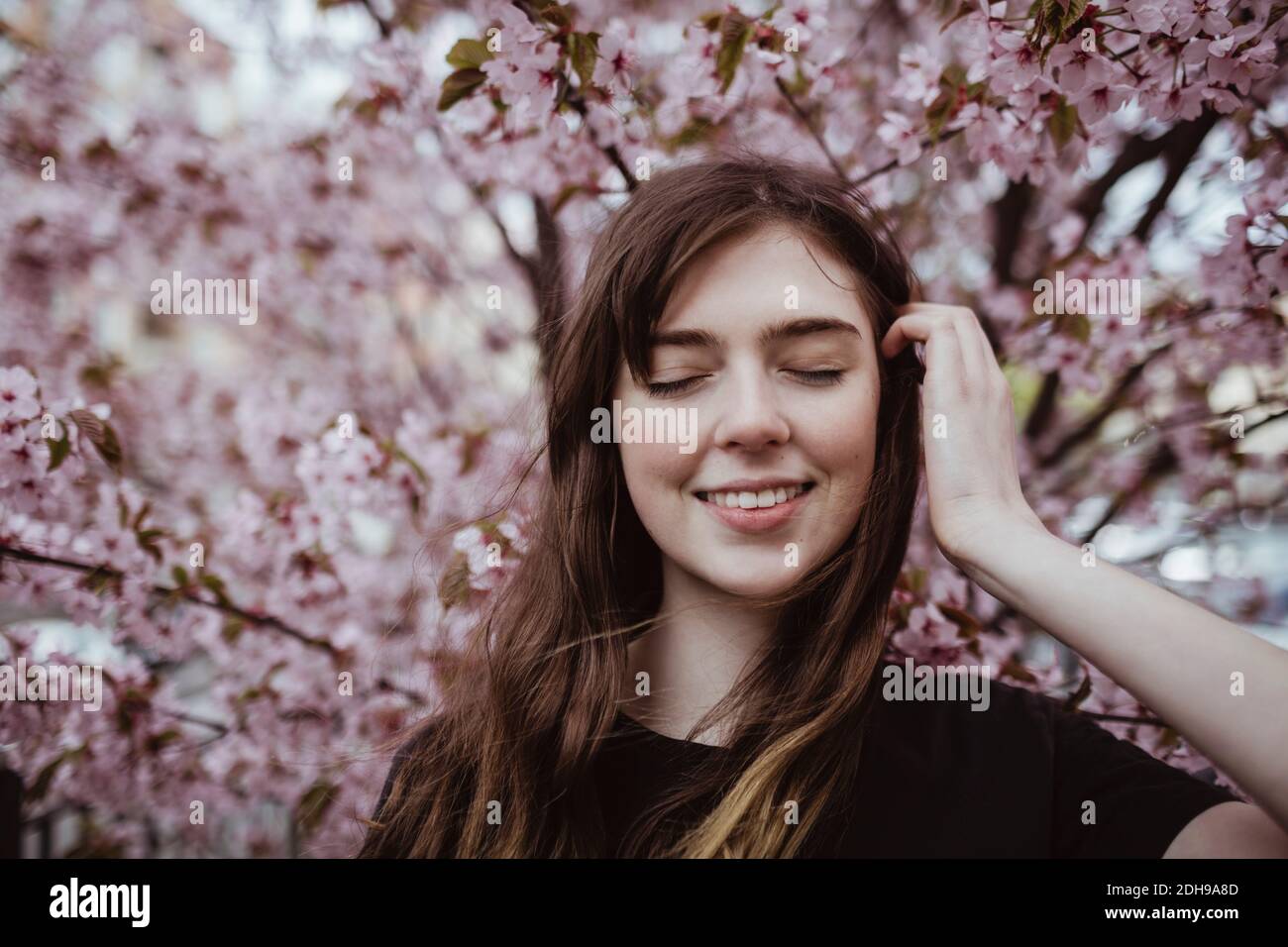 Femme souriante avec les yeux fermés debout contre l'arbre Banque D'Images