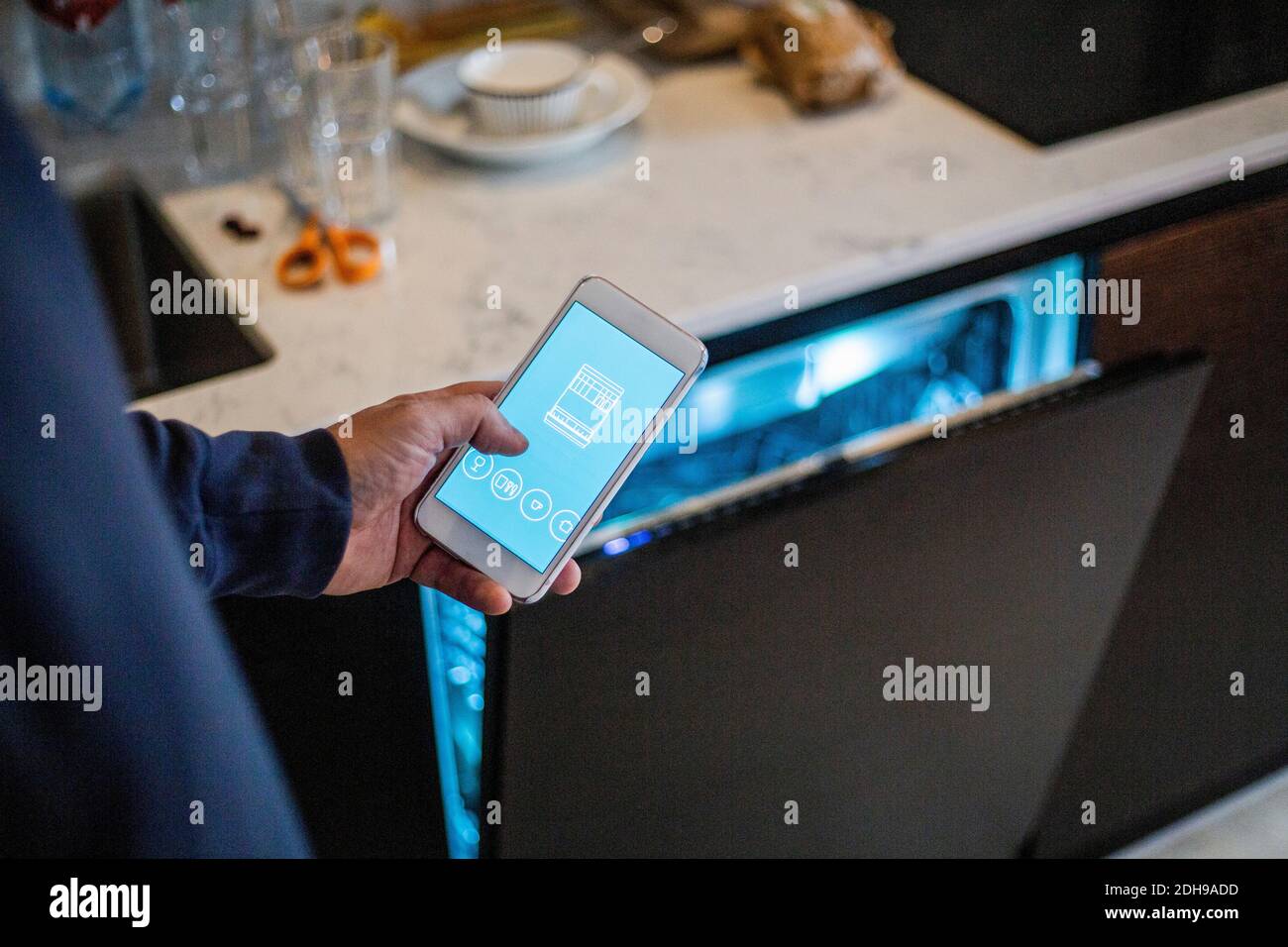 Image rognée de l'homme à l'aide de l'application mobile contre le lave-vaisselle à maison intelligente Banque D'Images
