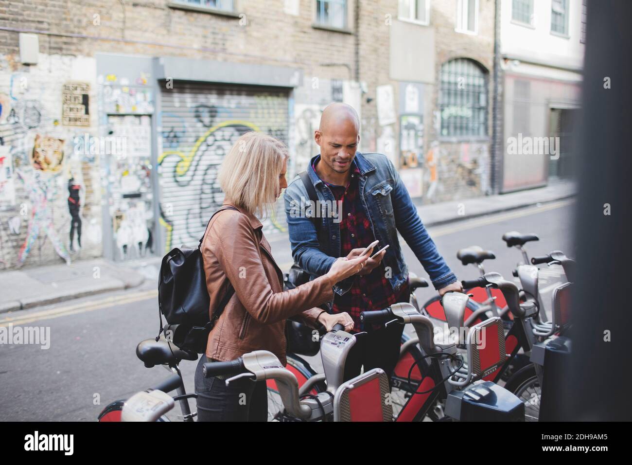 Couple utilisant des téléphones mobiles au système de partage de vélos Banque D'Images