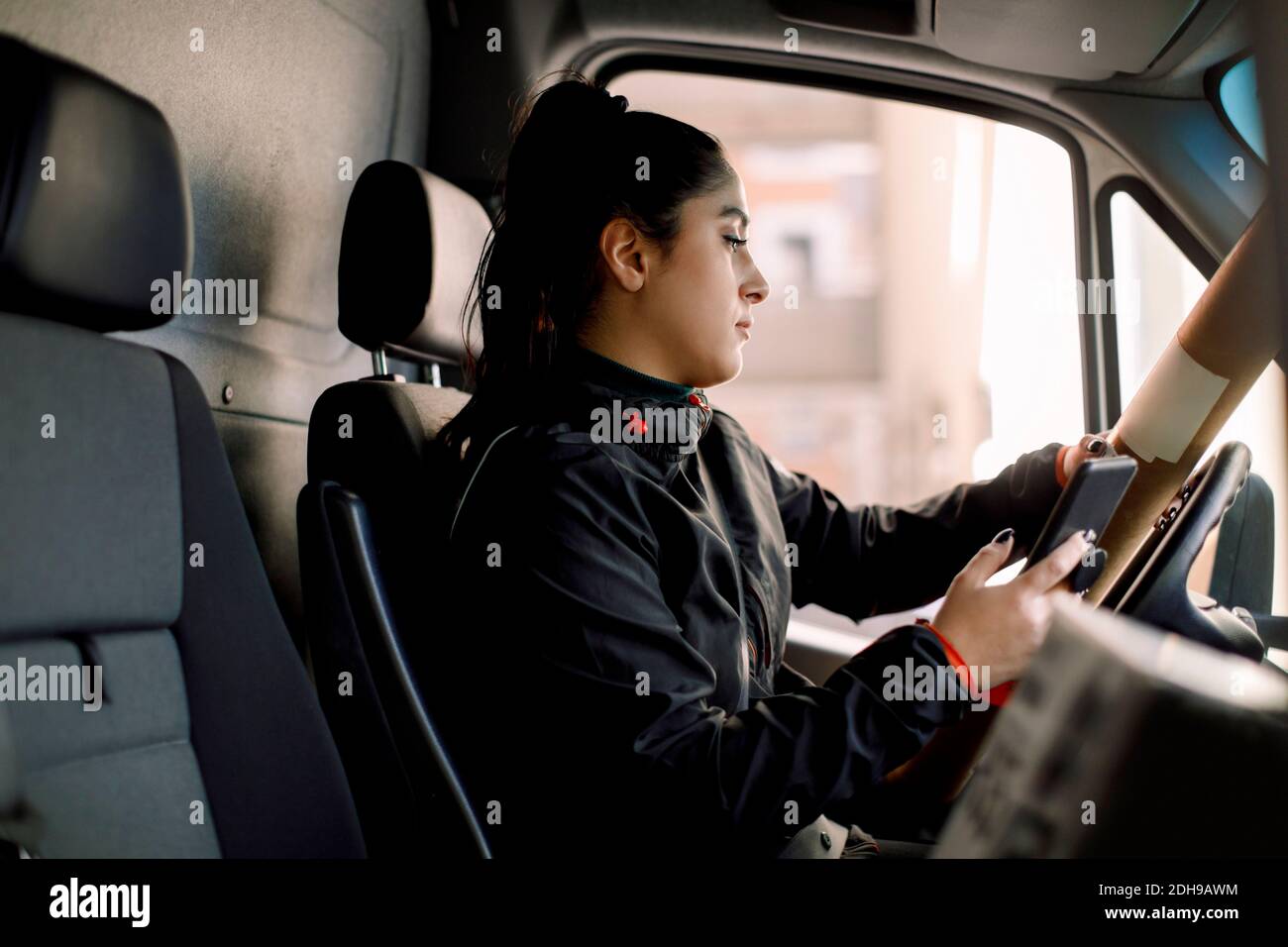 Femme de livraison avec colis utilisant un smartphone en conduisant un camion Banque D'Images