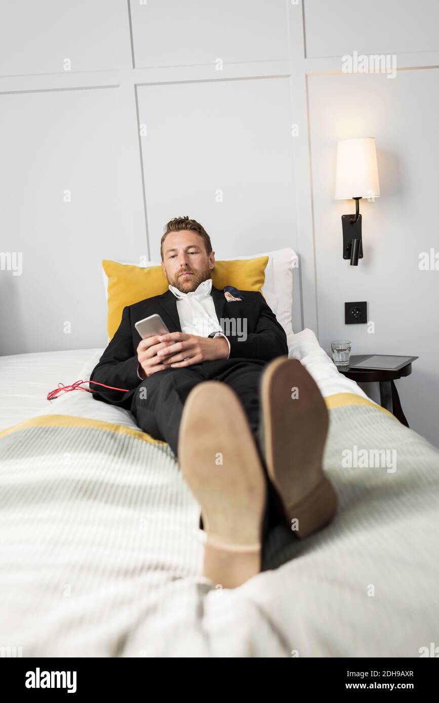 Homme d'affaires se détendant au lit tout en écoutant de la musique depuis son mobile téléphone dans la chambre d'hôtel Banque D'Images
