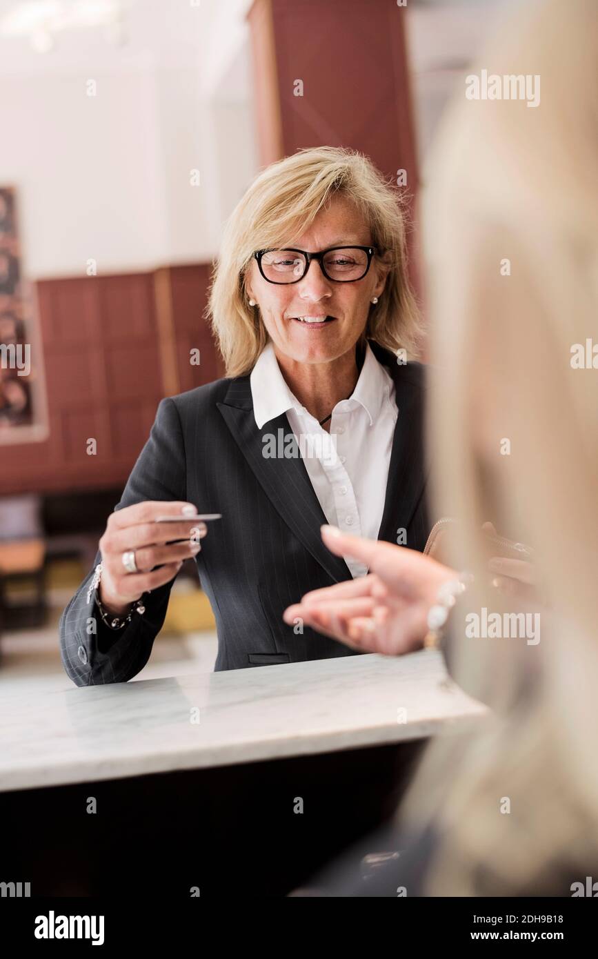 Bonne femme d'affaires mûre, réceptionniste payant avec carte de crédit à l'hôtel paiement Banque D'Images