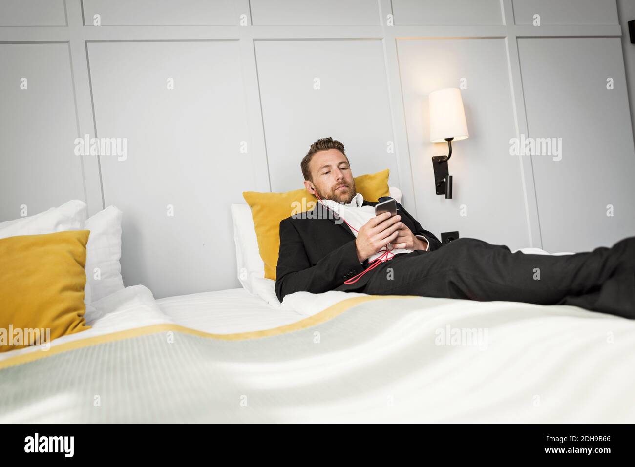 Homme d'affaires allongé sur le lit tout en écoutant de la musique depuis son mobile téléphone dans la chambre d'hôtel Banque D'Images