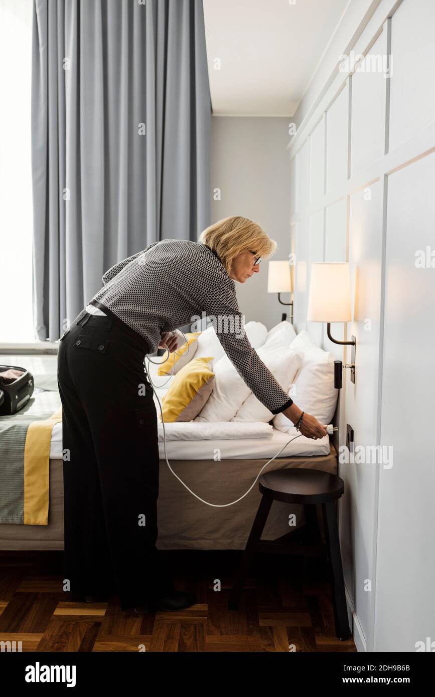 Femme d'affaires qui branche le câble près du lit dans la chambre d'hôtel Banque D'Images