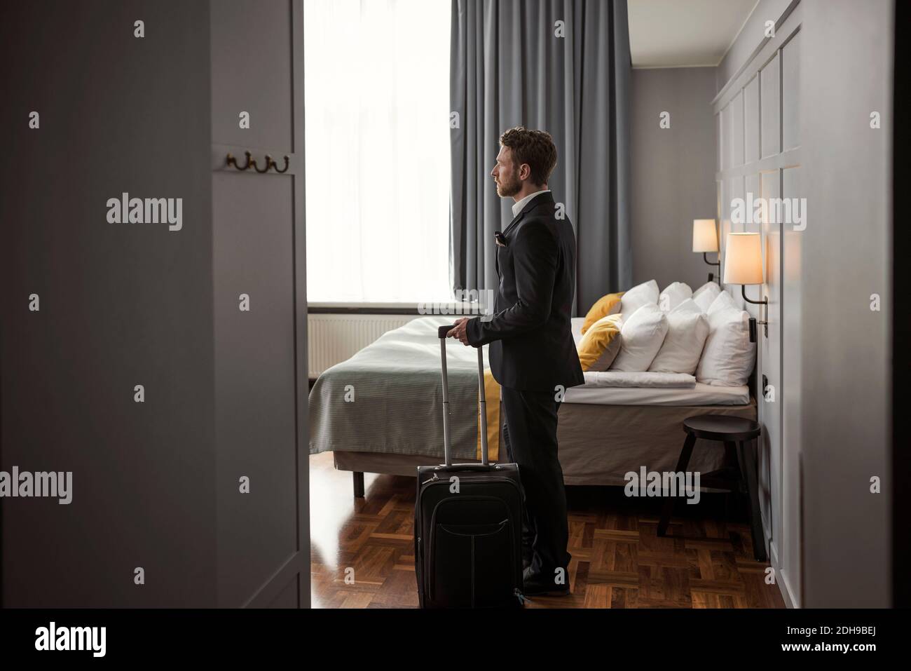 Vue latérale d'un homme d'affaires debout avec ses bagages au lit chambre d'hôtel Banque D'Images