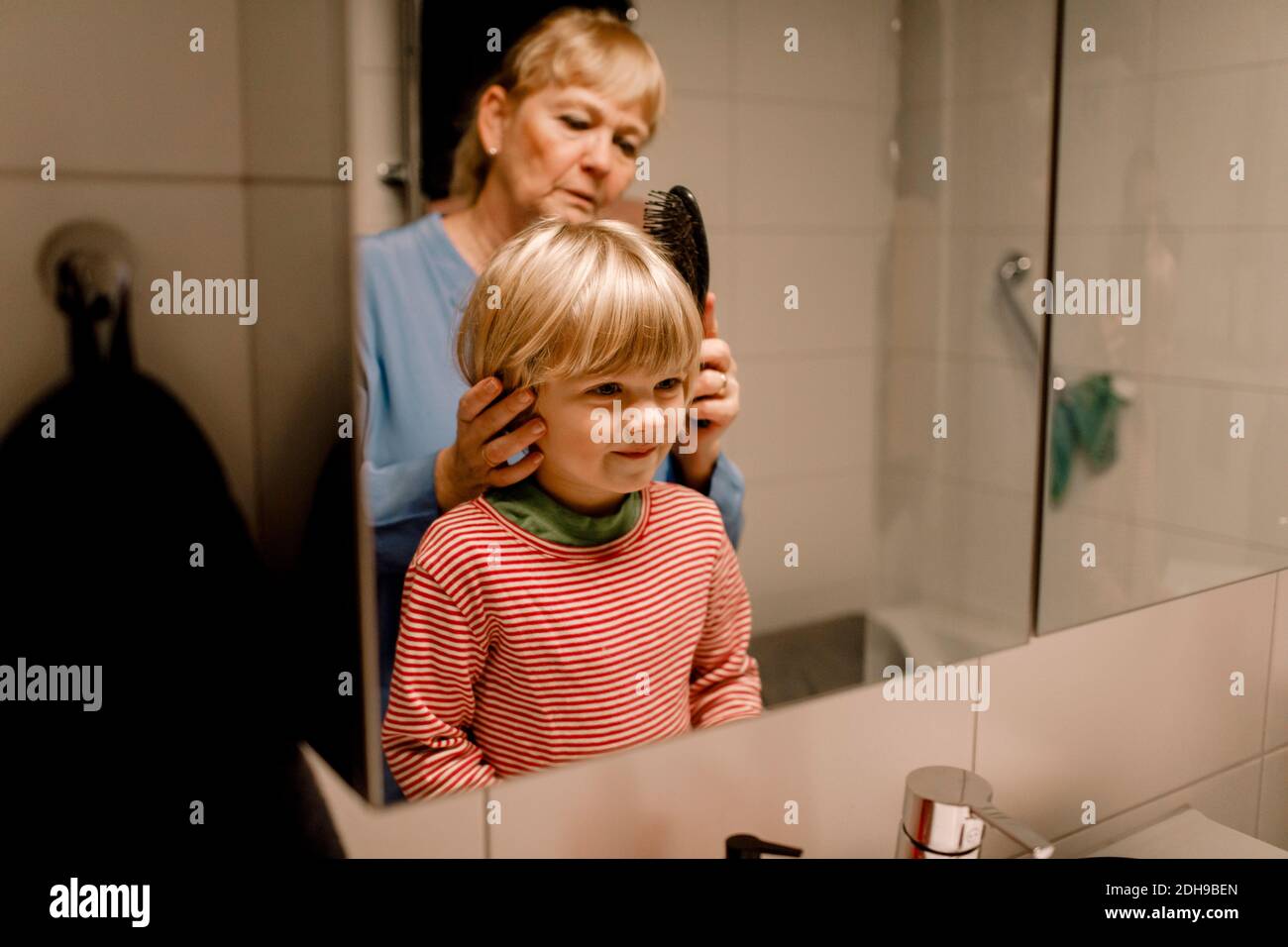 Femme âgée peignant les cheveux de petit-fils dans la salle de bains à la maison Banque D'Images