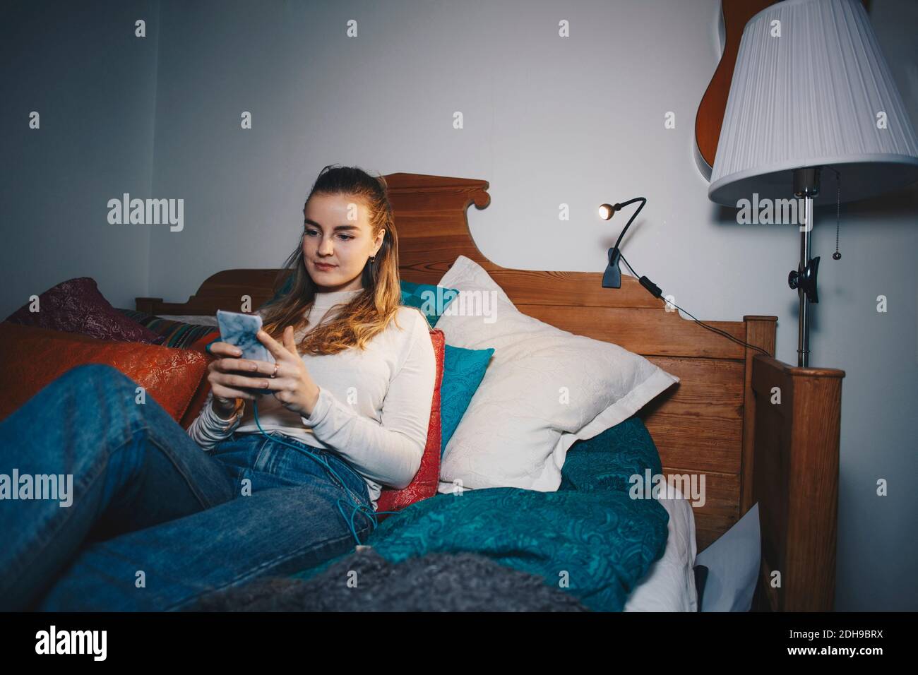Jeune femme assise sur le lit à l'aide d'un téléphone portable dans un dortoir chambre Banque D'Images