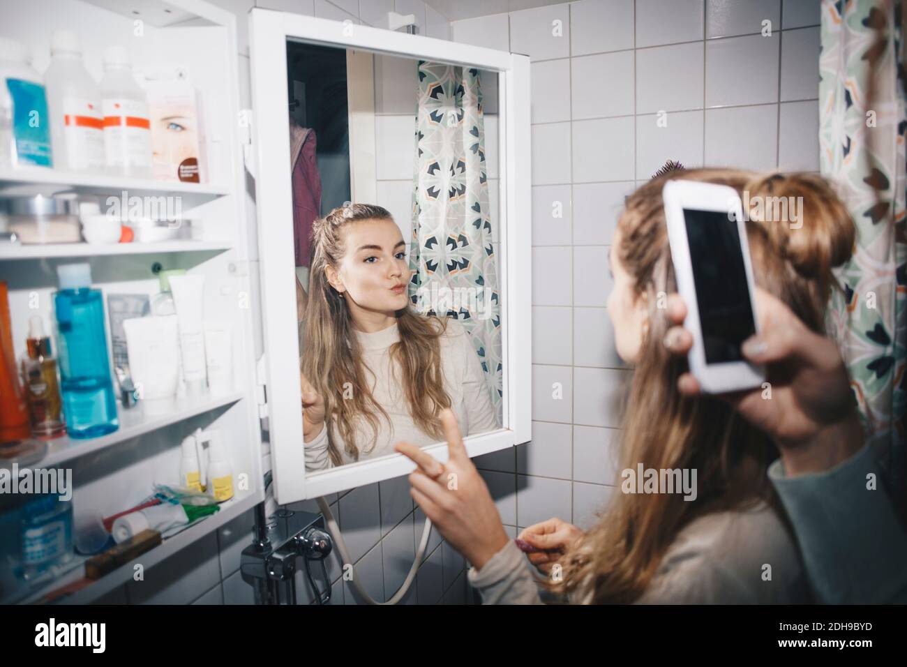 Main rognée de la femme photographiant une amie féminine dans un miroir au dortoir salle de bains Banque D'Images