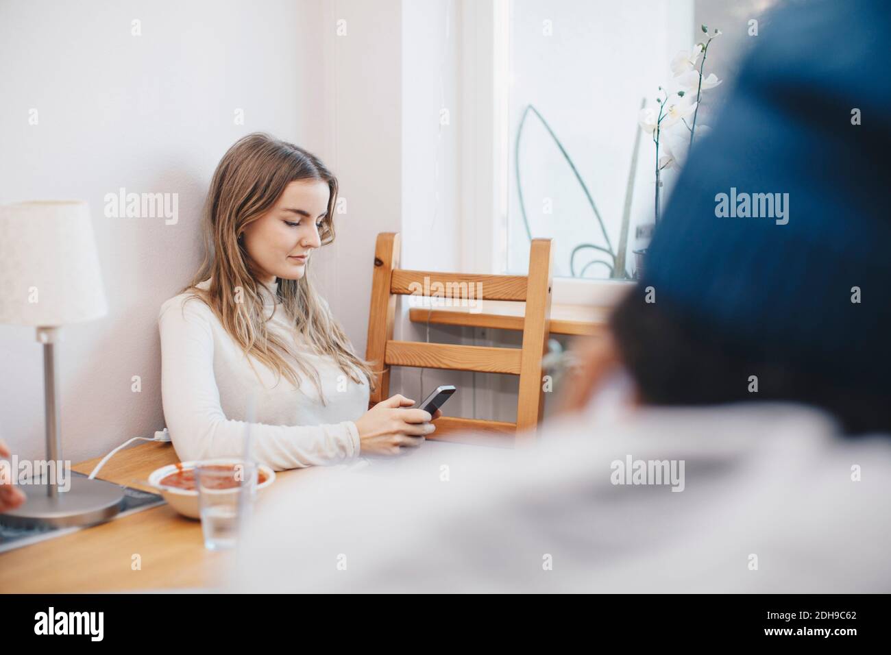 Femme utilisant un téléphone portable assis à la table contre le mur à l'intérieur dorm Banque D'Images