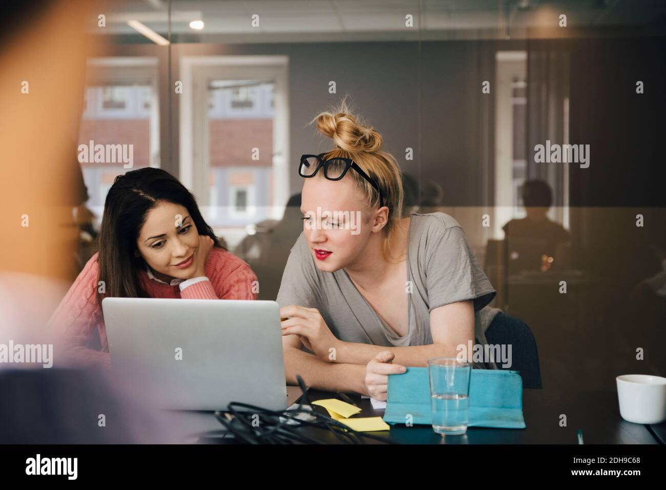 Femme d'affaires discutant avec un collègue transgenre au-dessus d'un ordinateur portable dans la salle de bord pendant la réunion Banque D'Images