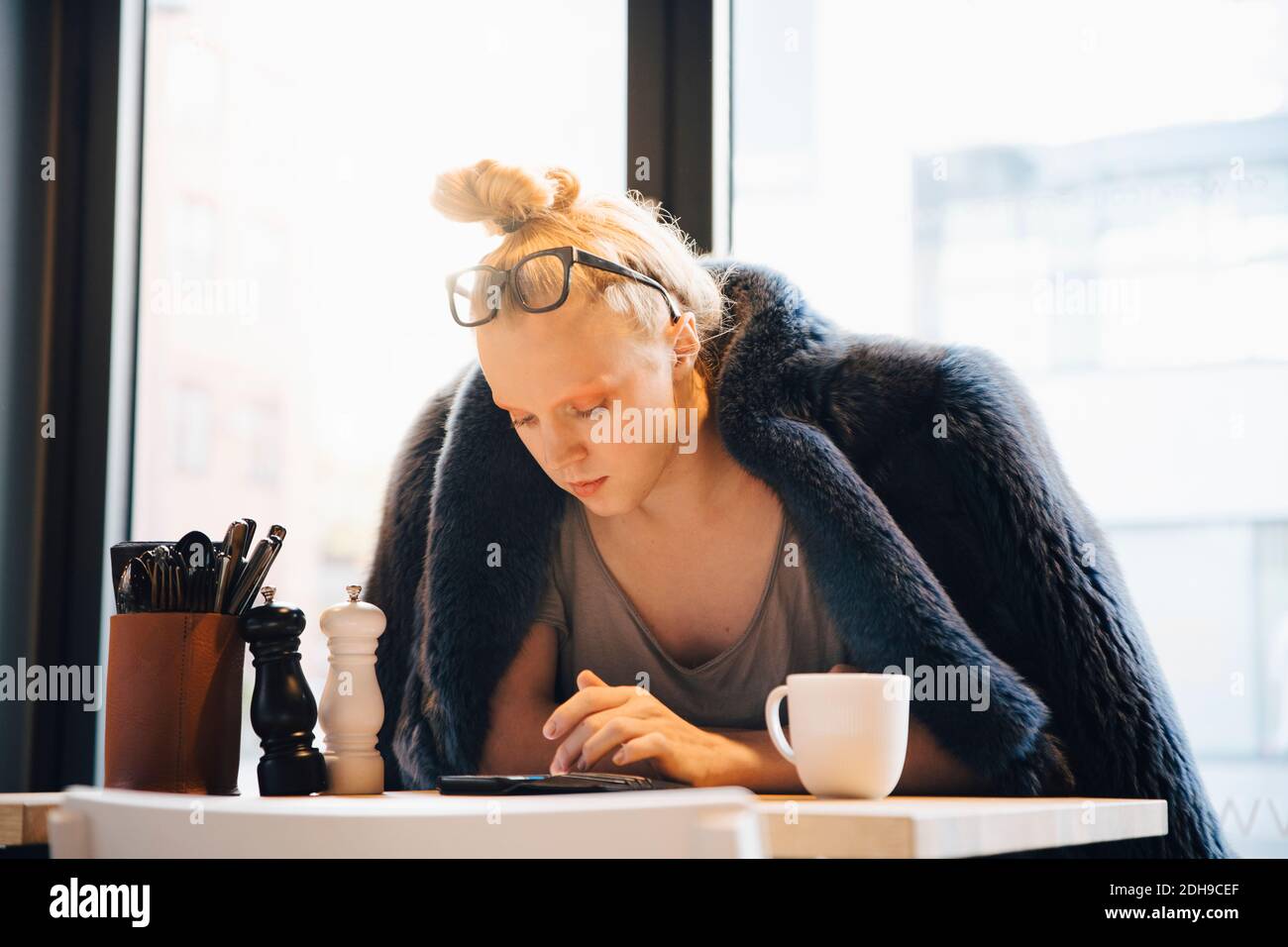 Jeune client transgenre utilisant un smartphone assis à une table dans le café Banque D'Images