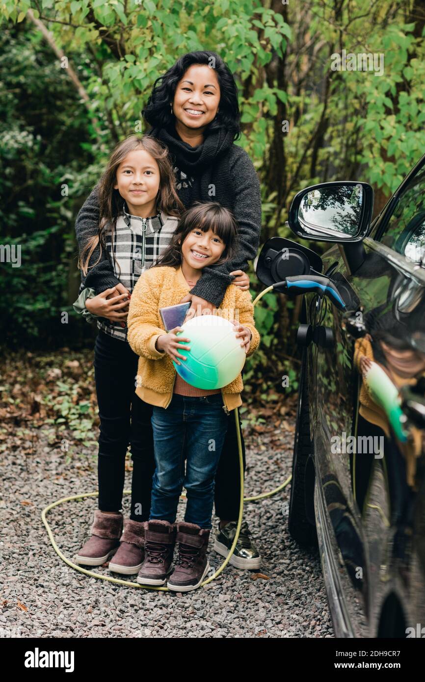 Portrait d'une femme souriante avec des filles en voiture électrique à station de charge Banque D'Images
