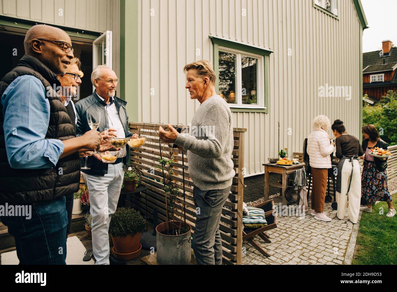 Les hommes âgés parlent et apprécient les collations pendant que les femmes préparent dîner dans la cour arrière Banque D'Images