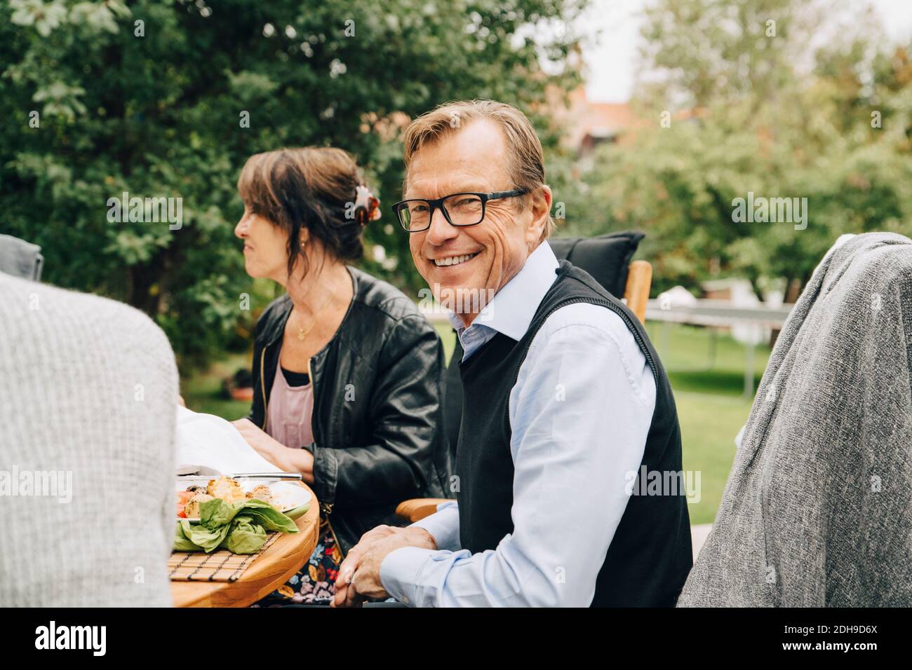 Portrait d'un homme âgé souriant assis avec des amis au restaurant table dans la cour arrière Banque D'Images