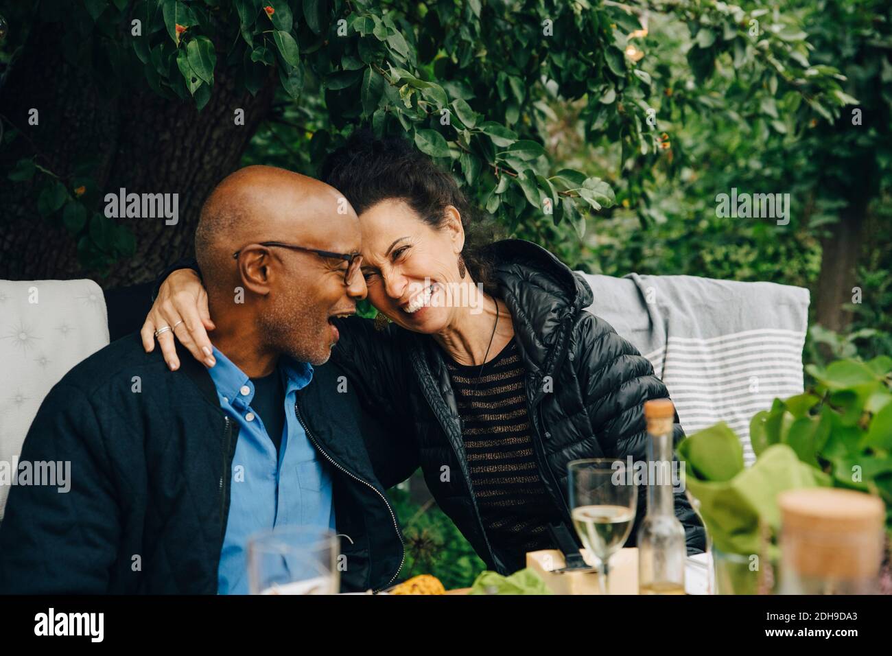 Homme et femme âgés joyeux appréciant tout en étant assis à dîner table pendant la fête dans le jardin Banque D'Images