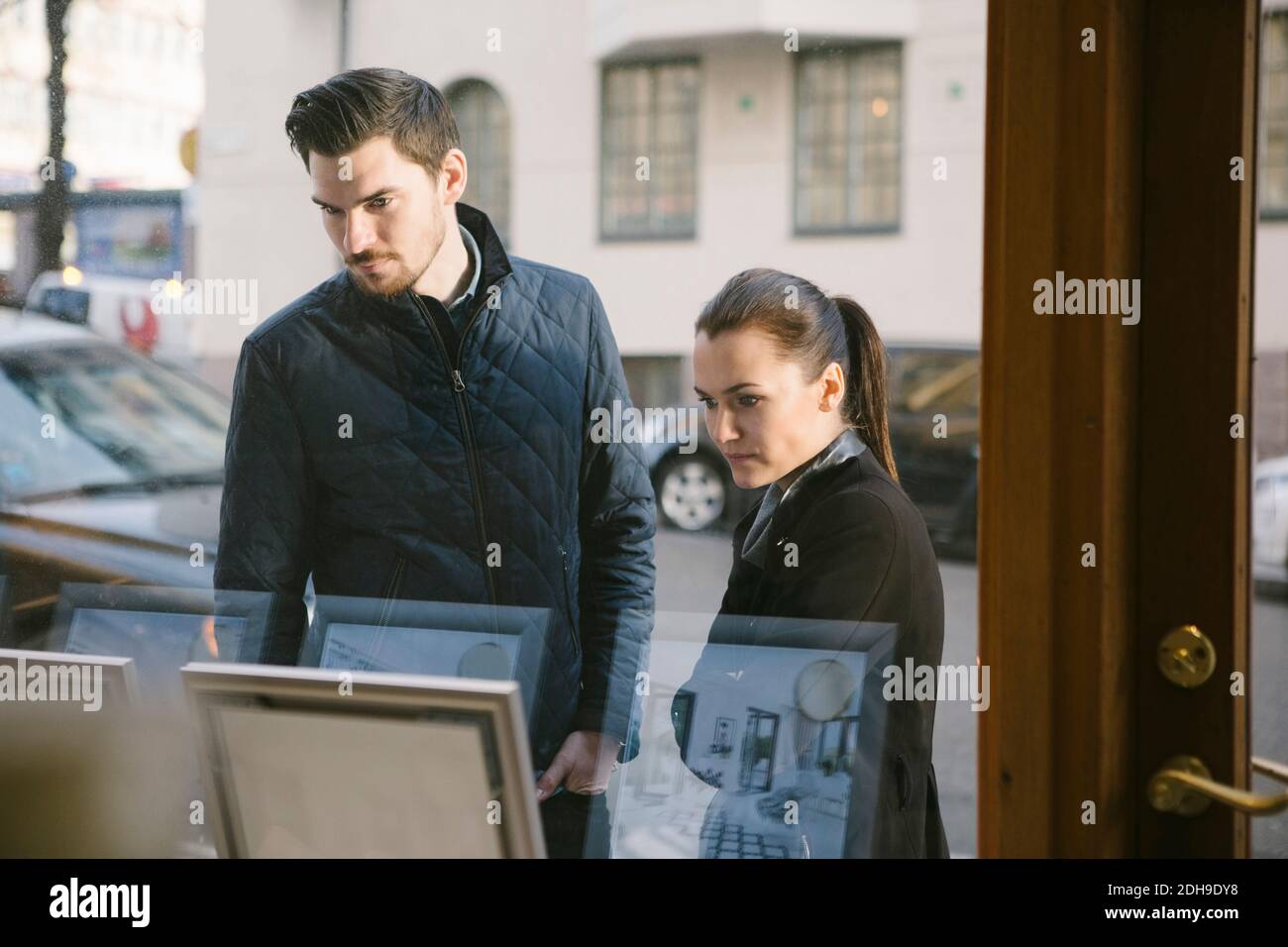 Jeune couple regardant des cadres d'image sur l'écran vu de fenêtre office Banque D'Images