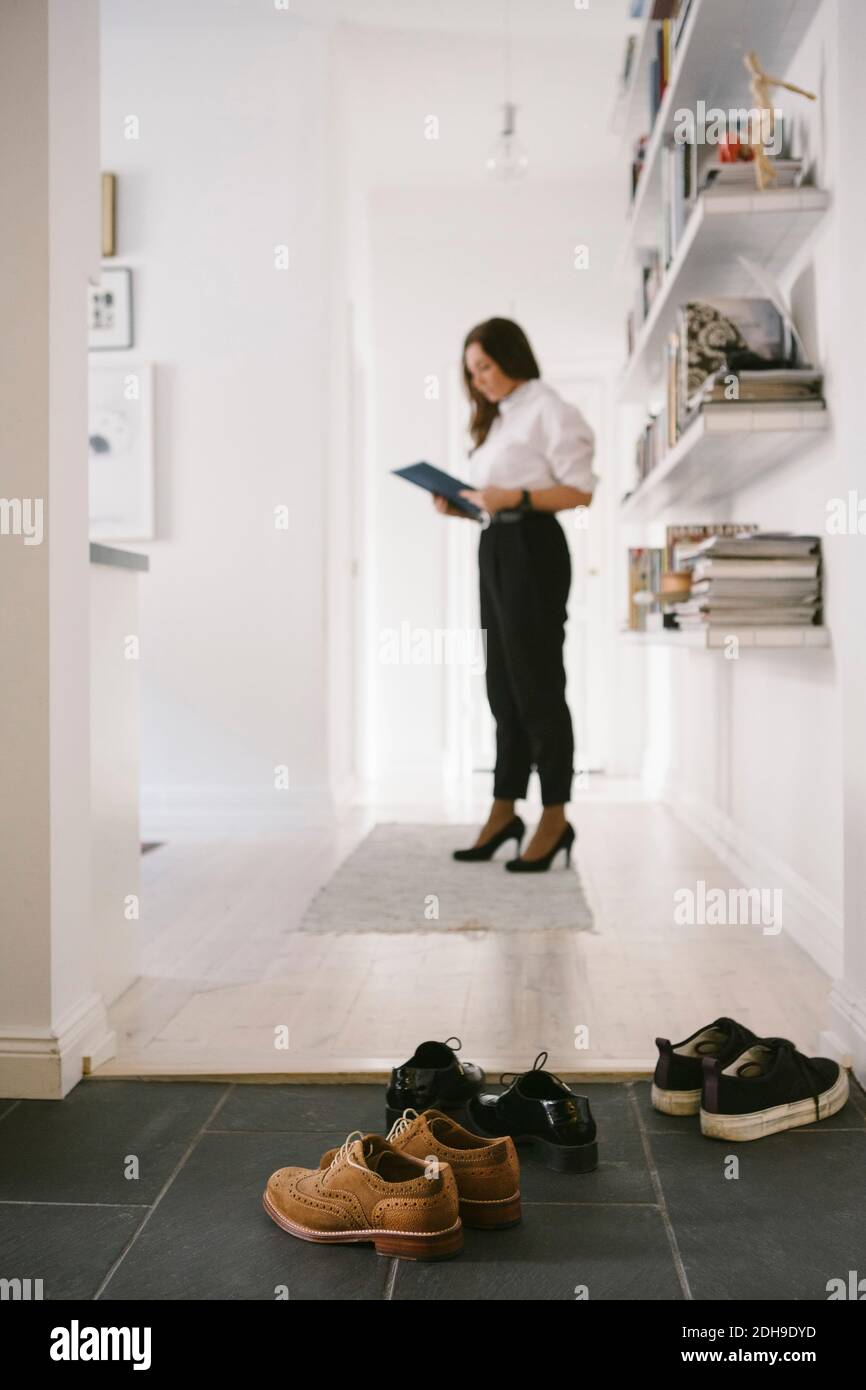Différentes chaussures sur le sol avec femme Realtor lire la brochure par étagères en arrière-plan Banque D'Images