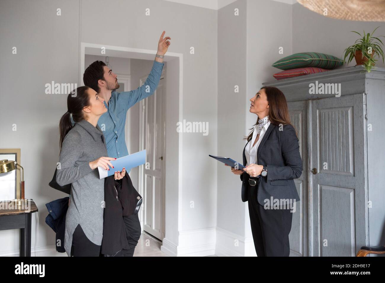 Femme et femme Realtor regardant l'homme pointant vers le haut pendant debout dans la chambre Banque D'Images