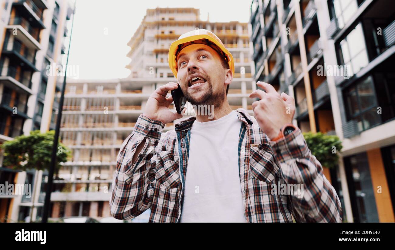 Un constructeur en colère, insatisfait de la date limite de travail, se met à l'épreuve en parlant au contremaître sur fond téléphonique de construction Banque D'Images