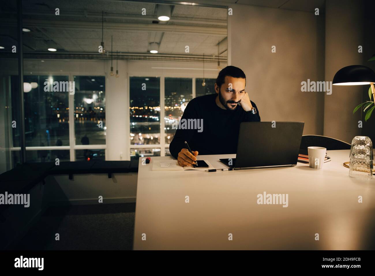 Homme d'affaires fatigué travaillant tard tout en étant assis au bureau éclairé bureau créatif Banque D'Images