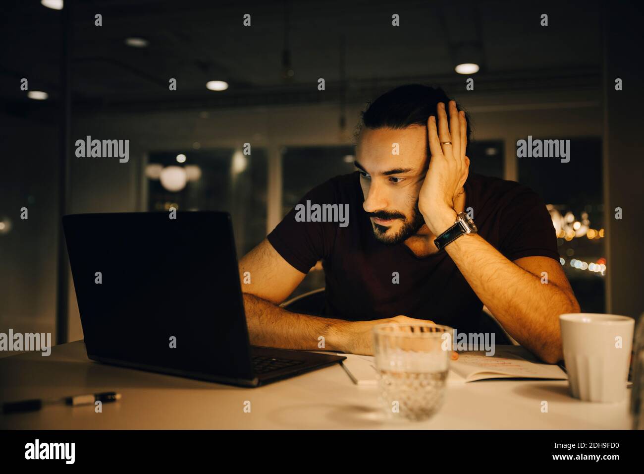 Homme d'affaires fatigué travaillant tard tout en regardant un ordinateur portable allumé bureau Banque D'Images