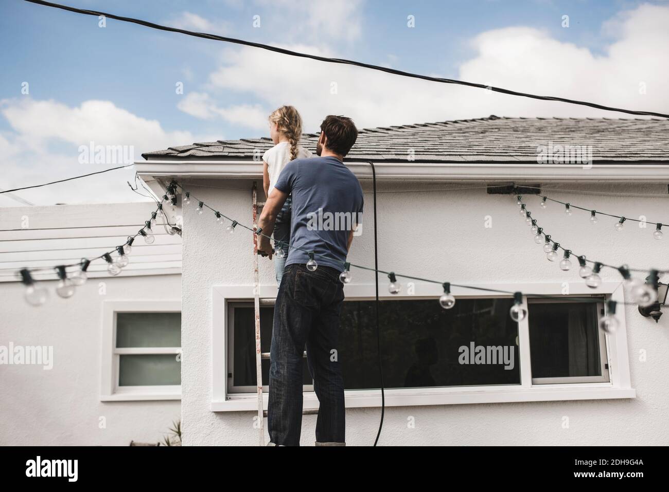 Vue arrière de l'homme avec sa fille grimpant sur l'échelle à maison Banque D'Images