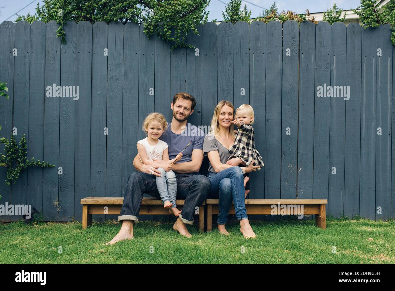 Portrait complet de parents heureux et d'enfants assis sur sièges contre la clôture dans la cour Banque D'Images