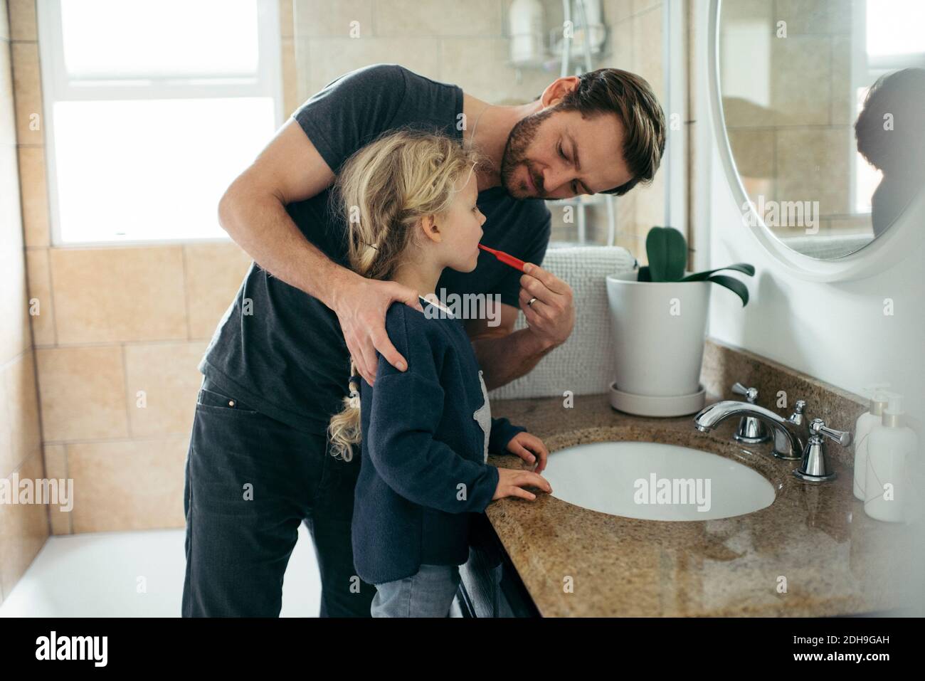 Un père d'un âge moyen se brossant les dents de sa fille au lavabo de la salle de bains Banque D'Images