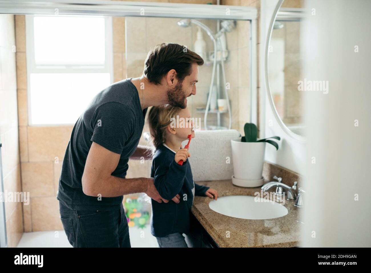 Vue latérale d'un père qui regarde sa fille se brosser les dents dans l'évier dans la salle de bains Banque D'Images