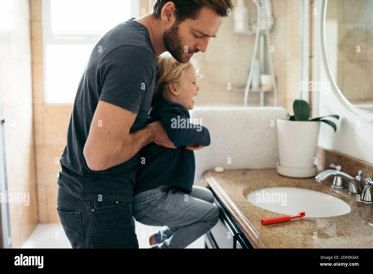 Vue latérale du père transportant sa fille au lavabo de la salle de bains Banque D'Images