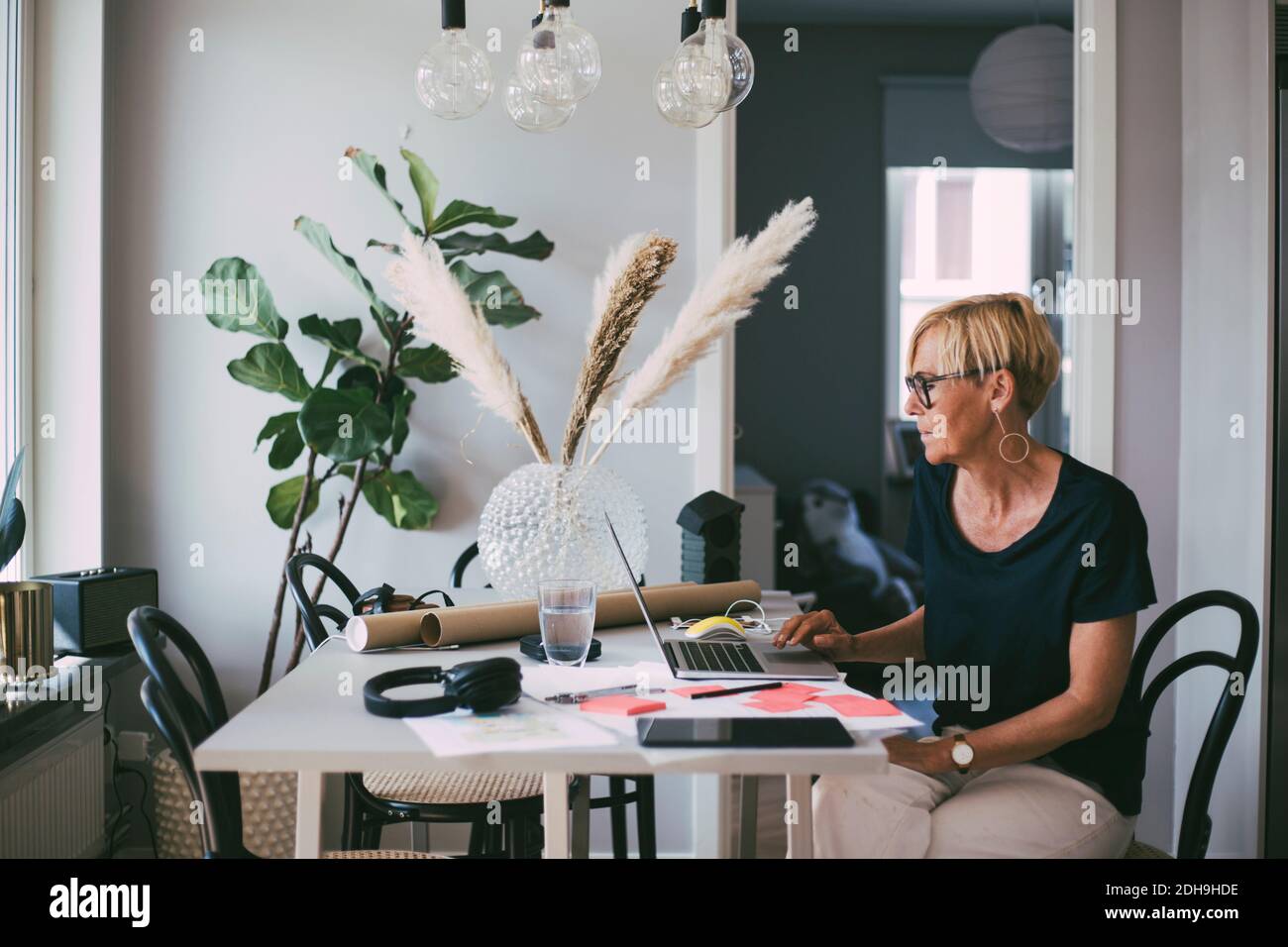 Femme travaillant à la maison assise à table lisant sur un ordinateur portable écran Banque D'Images