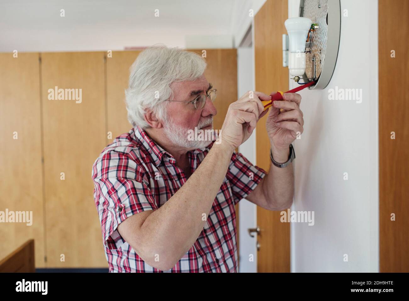 Homme senior répare les sconce avec un tournevis à la maison Banque D'Images