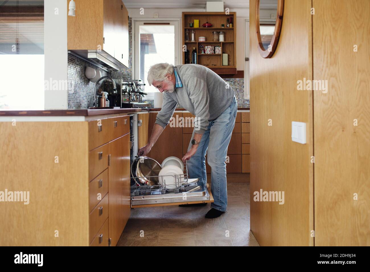 Homme senior mettant des plaques au lave-vaisselle dans la cuisine Banque D'Images