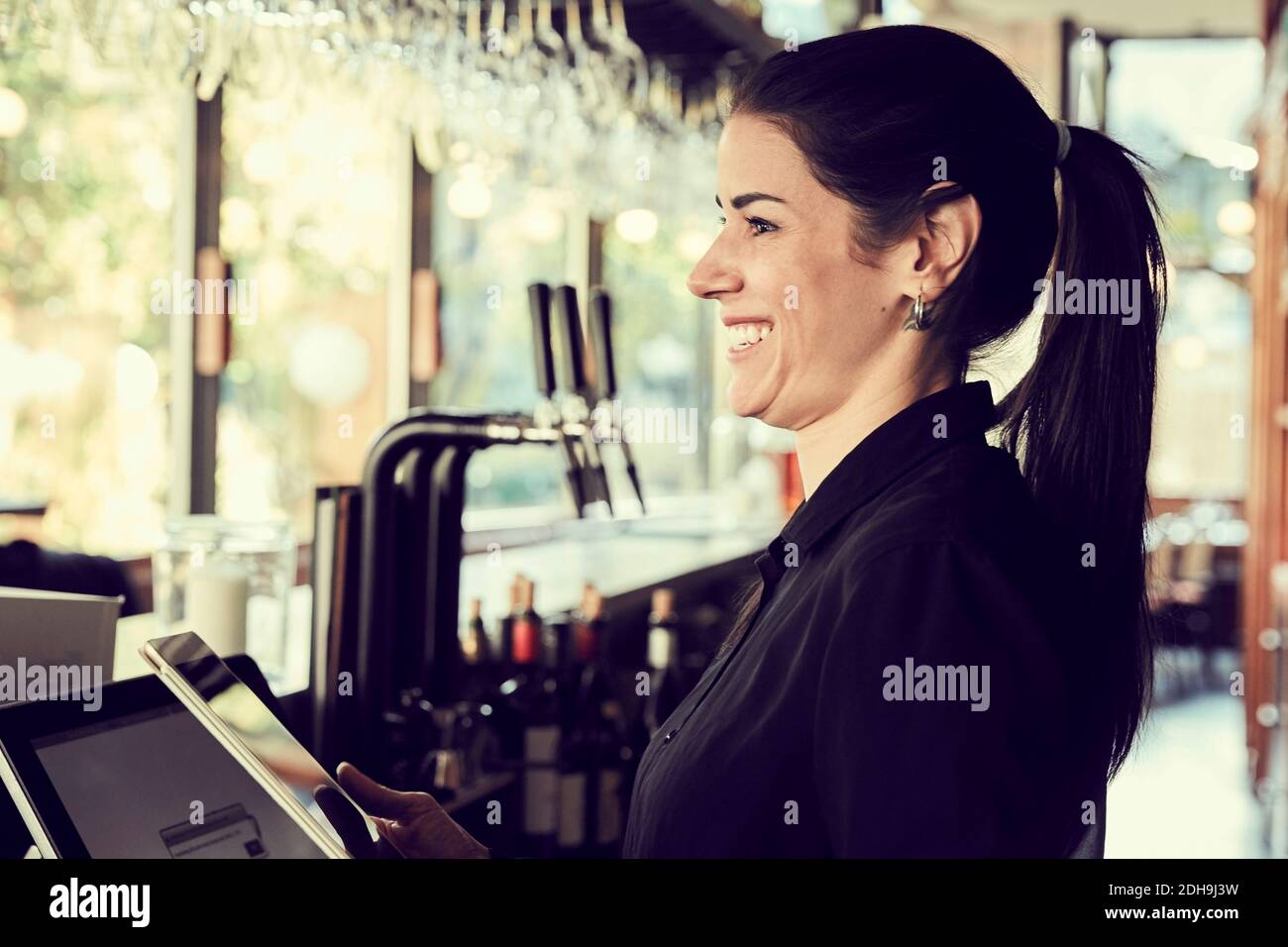 Femme souriante avec une tablette numérique qui regarde loin en se tenant debout dans le café Banque D'Images