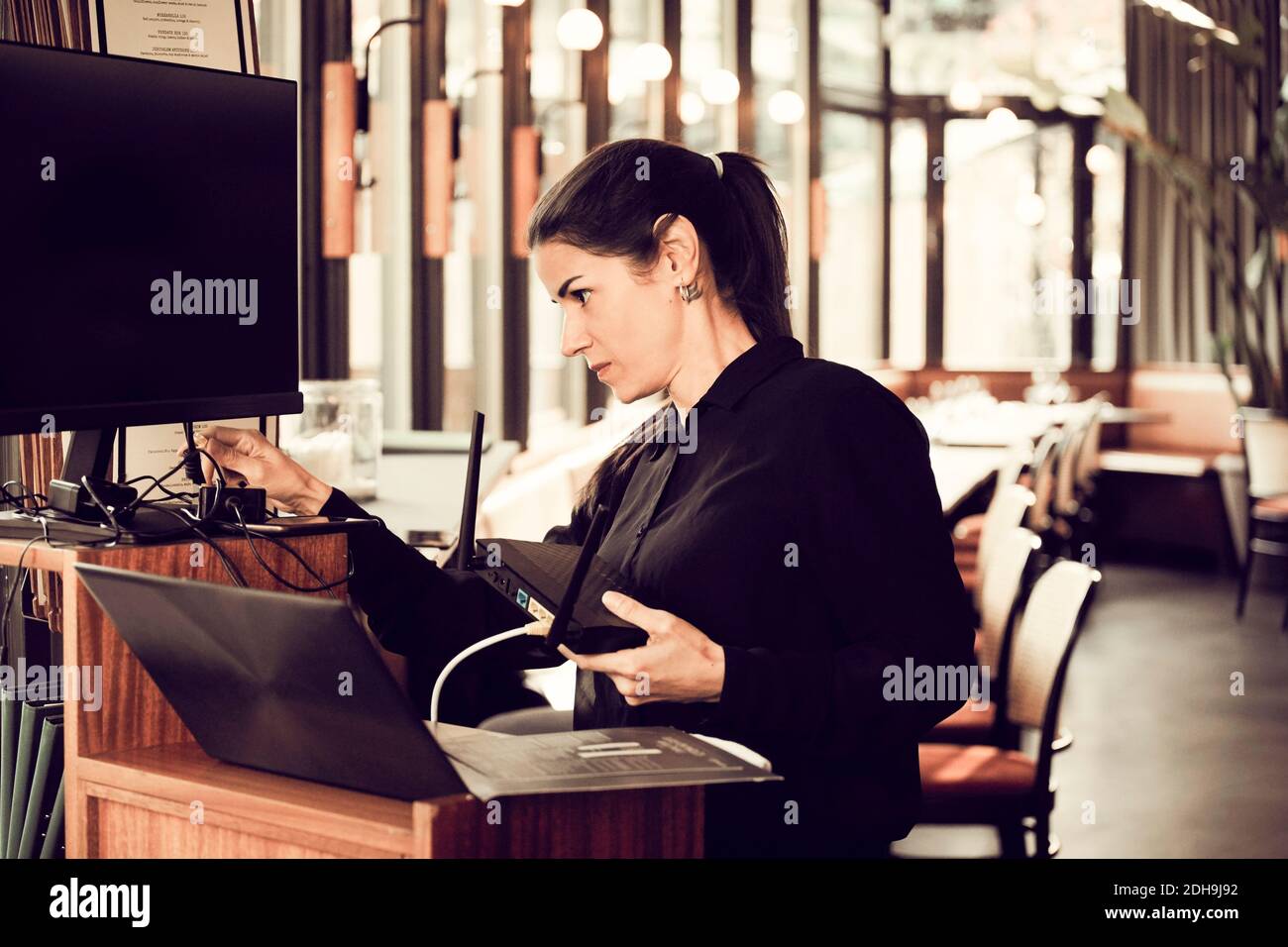 Femme propriétaire câble d'ajustement de moniteur d'ordinateur dans le café Banque D'Images