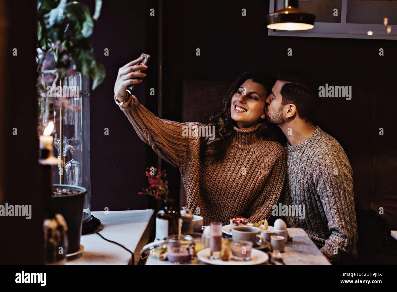 Femme souriante qui prend le selfie à travers un smartphone alors qu'elle est une partenaire masculine embrasser à l'hôtel Banque D'Images