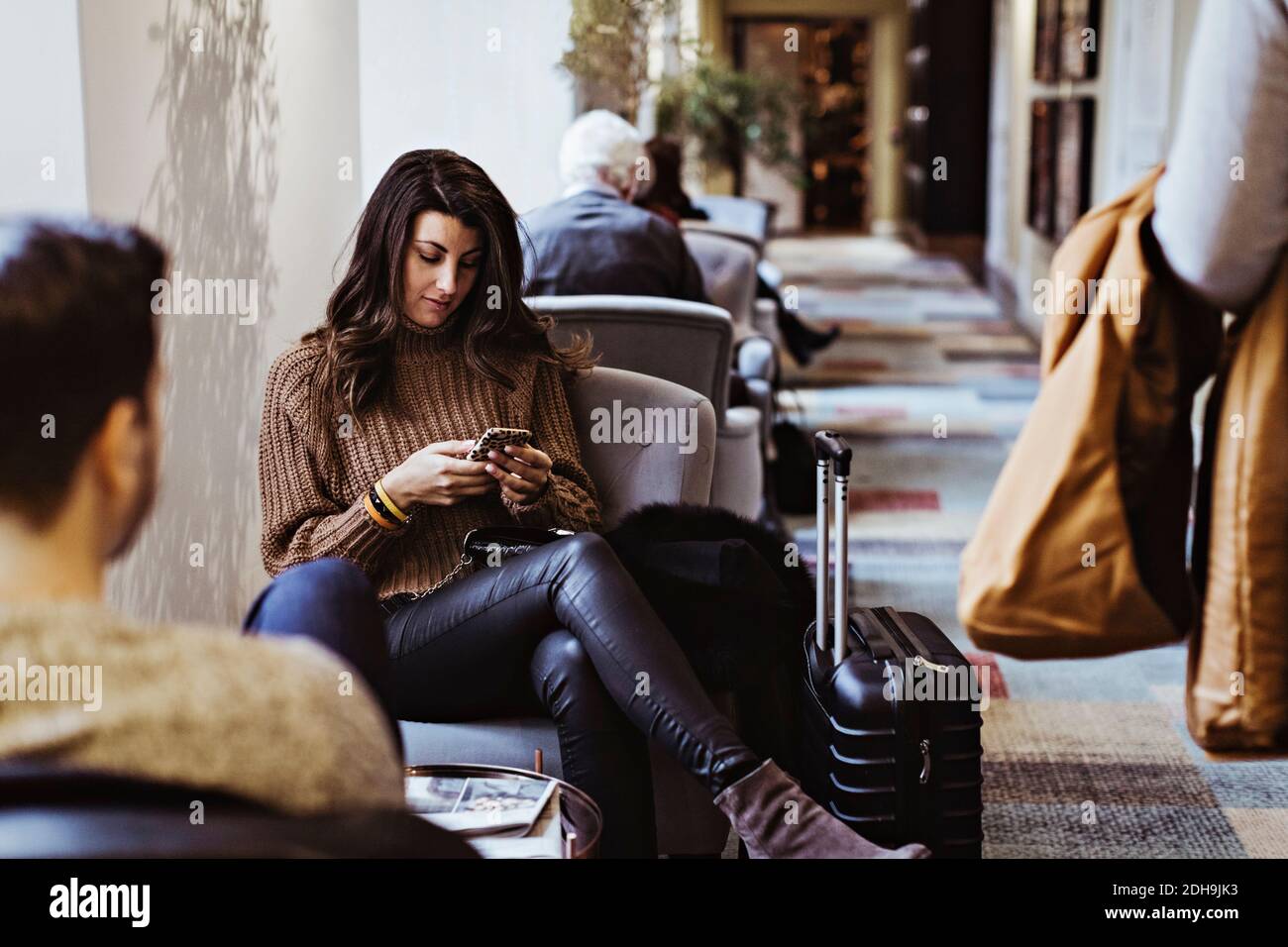 Femme adulte de taille moyenne utilisant un téléphone portable assis devant de petit ami à l'hôtel Banque D'Images
