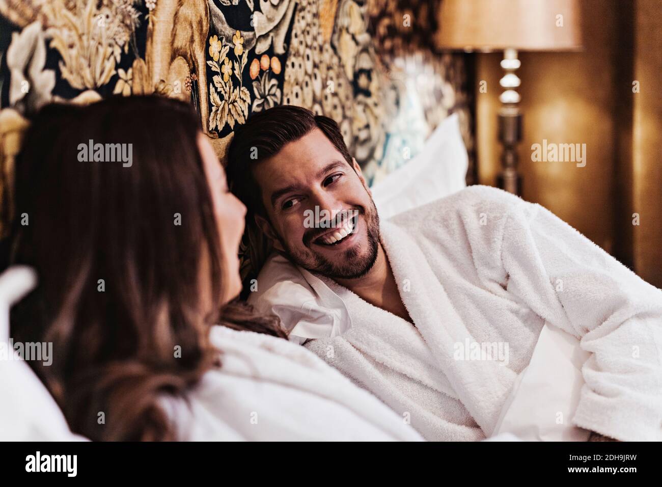 Joyeux homme moyen adulte parlant avec une petite amie tout en se relaxant lit dans la chambre d'hôtel Banque D'Images