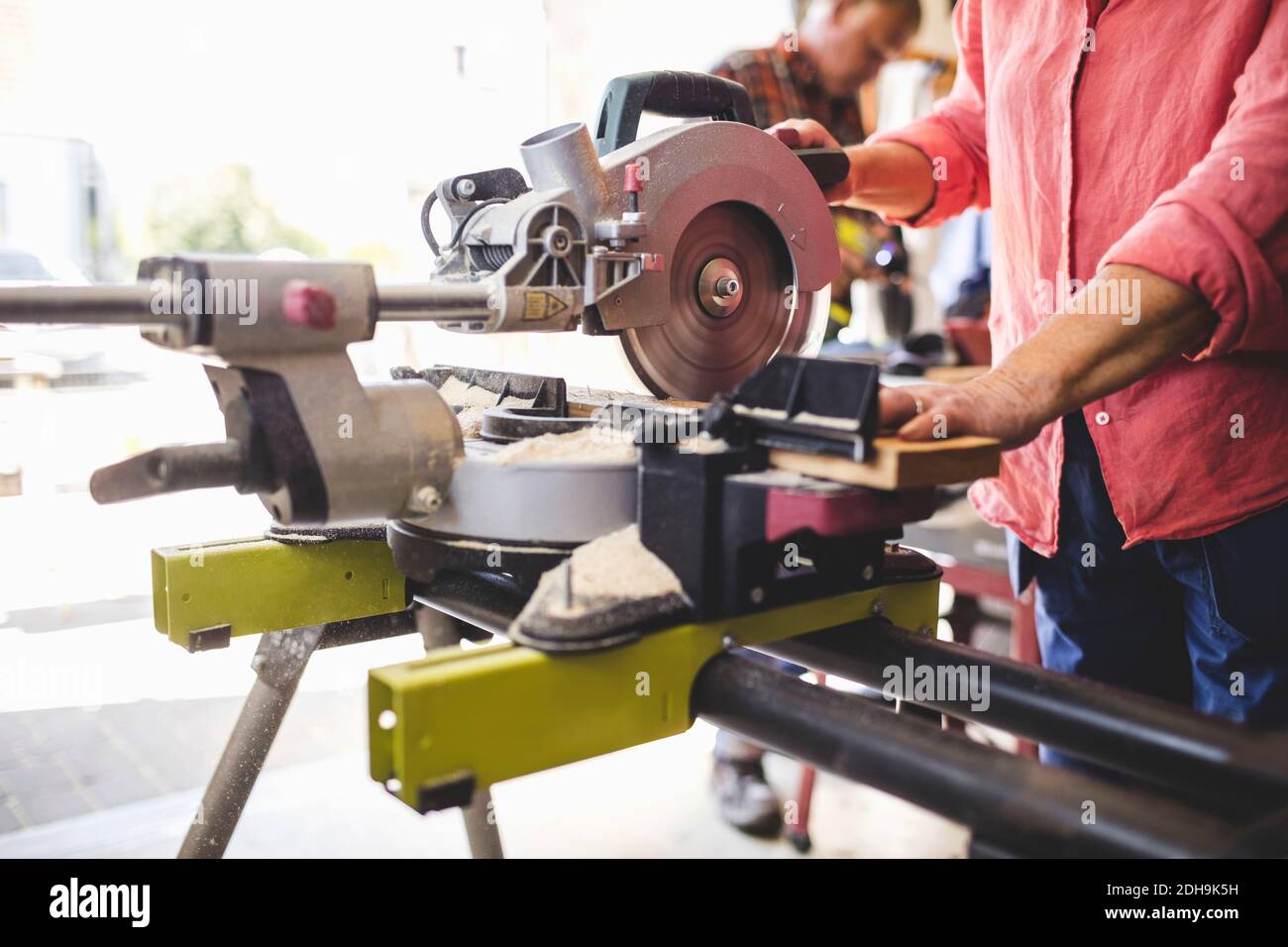 Section médiane d'une femme âgée coupant une planche en bois avec une scie circulaire à l'atelier Banque D'Images
