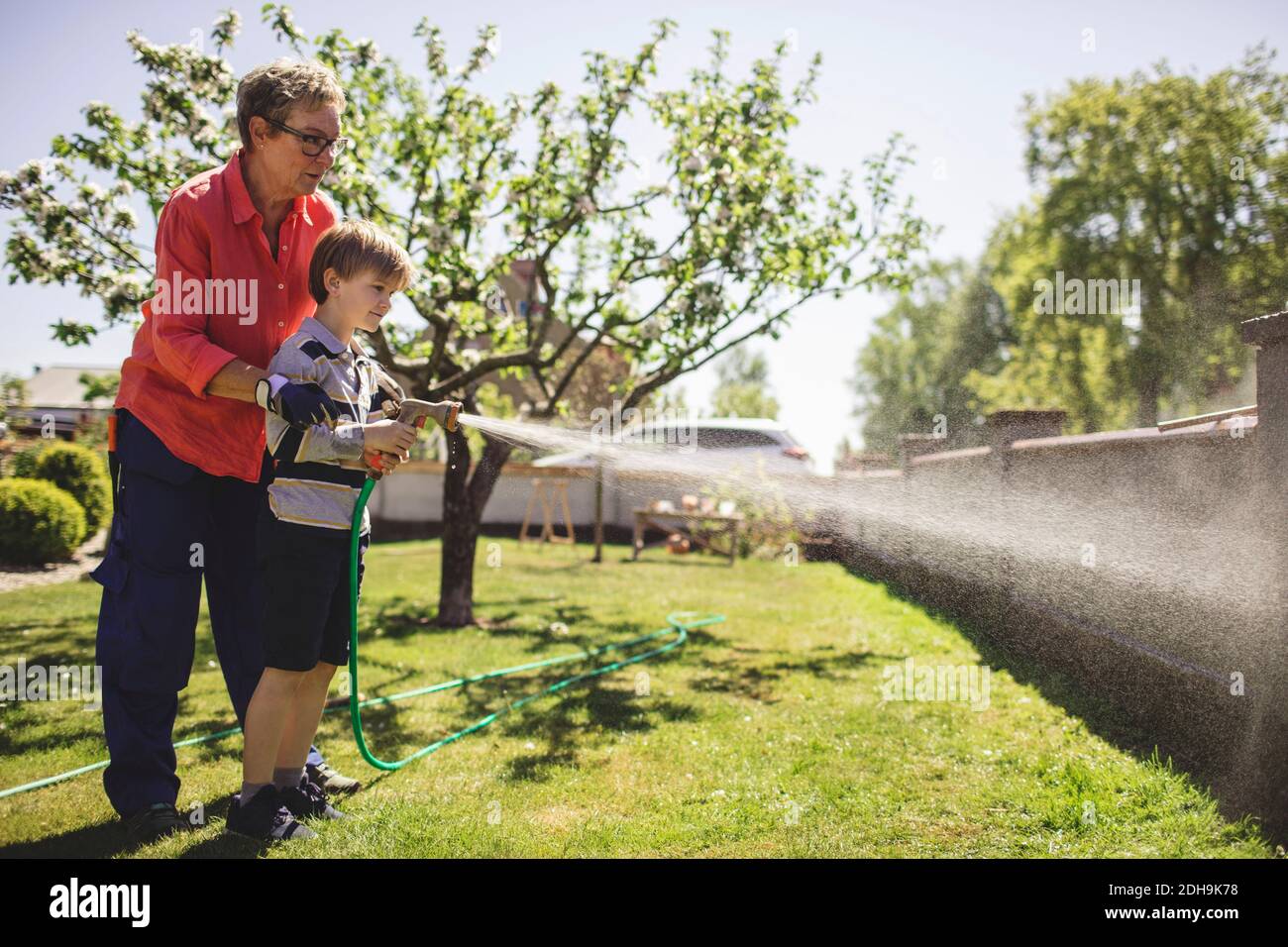Une grande-mère qui aide son petit-fils à pulvériser de l'eau mur environnant à la cour Banque D'Images Une grande-mère qui aide son petit-fils à pulvériser de l'eau mur environnant à la cour Banque D'Images