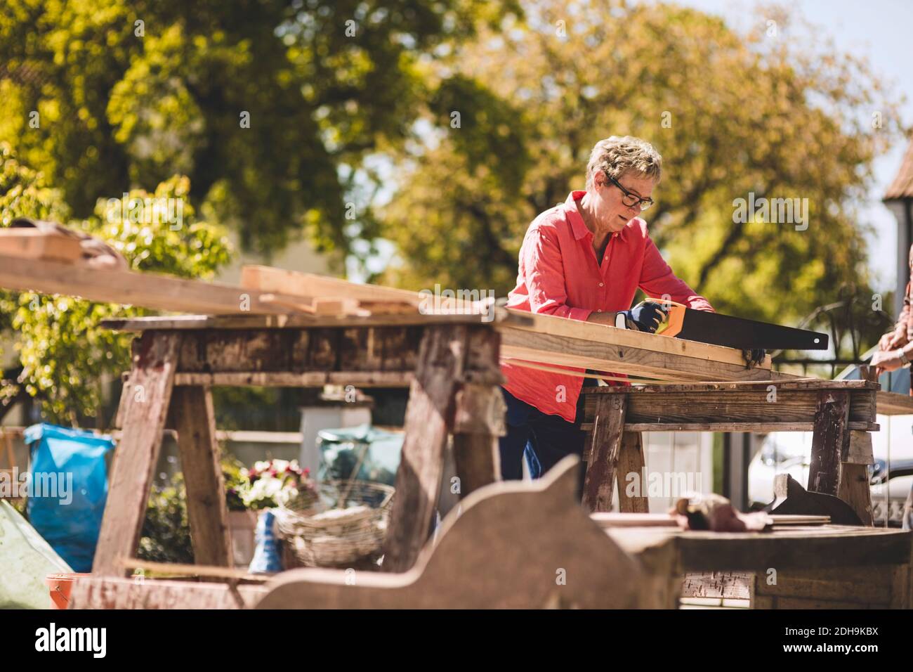 Femme âgée coupant une planche de bois avec une scie à main dans la cour Banque D'Images