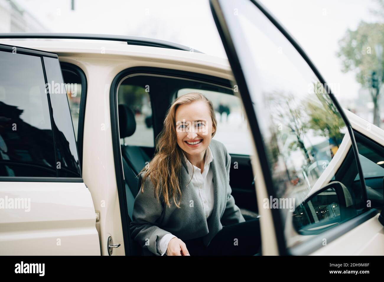 Femme entrepreneure souriante qui sort du taxi pendant un voyage d'affaires Banque D'Images