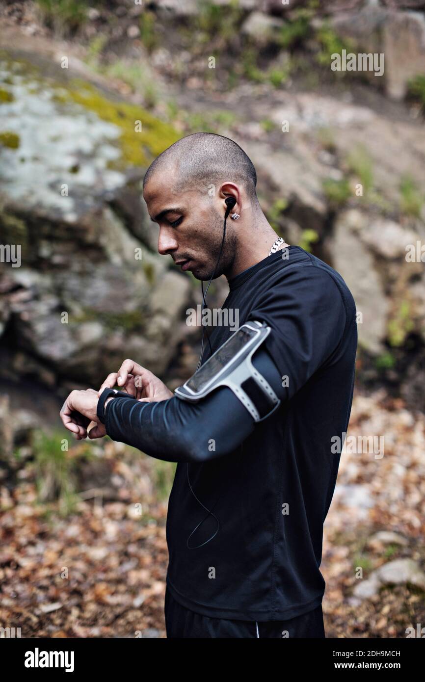 Vue latérale de l'athlète masculin vérifiant la montre intelligente dans la forêt Banque D'Images