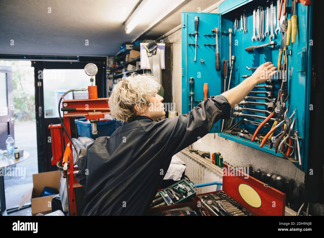 Un mécanicien de sexe féminin retire l'outil de travail de l'armoire lors de la réparation automatique boutique Banque D'Images